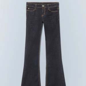Bootcut jeans från weekday  - Mörkblå bootcut jeans från weekday med låg midja och kontrasterande orange sömmar. Klassisk femficksmodell i jeansmaterial med coola detaljer som Cheap Monday-logga och säkerhetsnålar på bakfickan. Perfekta för dig som gillar retrovibbar och snygg passform.