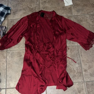 Vinröd spetsklänning från H&M XS/S - Vinröd kortklänning från H&M i glansig polyester med spetsdetaljer på axlar och ärmslut. Klänningen har trekvartsärm, omlottknytning i midjan och en elegant, flowy känsla. Perfekt för dig som gillar romantiska vibes och snygga detaljer.