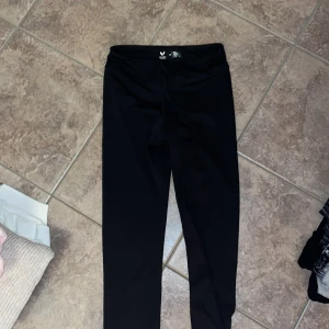 Svarta träningsleggings från SOC - Svarta leggings från SOC i stretchigt syntetmaterial, perfekta för träning. De har en smidig passform, hög midja och snörning i midjan för extra komfort. Snygga och enkla att matcha med din träningsgarderob.