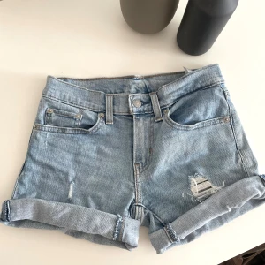 Levi's ljusblå jeansshorts - Snygga midwaist ljusblå jeansshorts från Levi's med klassisk femficksdesign, uppvikta benslut och slitna detaljer framtill. Sköna och stilrena shorts med normal passform.