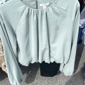 Ljusgrön blus från H&M - Säljer en ljusgrön blus från H&M med rund halsringning och långa ärmar. Blusen har en lös passform och är tillverkad i ett tunt, mjukt material. Knäppning i nacken med liten öppning baktill. Perfekt för en stilren look. Stl S