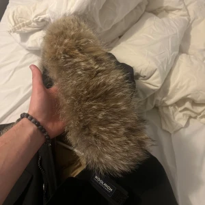 Svart Woolrich Arctic Parka med pälskrage - Säljer en svart Woolrich Arctic Parka med beige quiltat foder och avtagbar pälskrage. Jackan har flera praktiska fickor, dragkedja och knappar framtill. Perfekt för kalla dagar med sin dunfyllning och klassiska design.