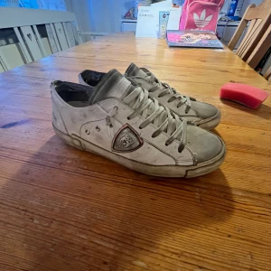 philpe models dom är rätt så slitna så kom med pris för slag vill bli av med dom - Säljer ett par vita sneakers från Philippe Model med grå detaljer och logotyp på sidan. Skorna har snörning och platt sula, samt en klassisk rund tå. Perfekta för en avslappnad och stilren look.