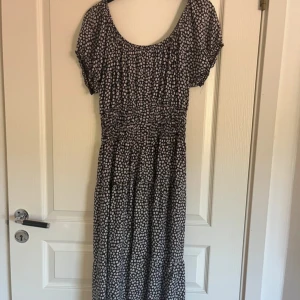 Blommig långklänning från Leana Mode - Supersöt långklänning med svart botten och små vita blommor från Leana Mode. Klänningen är offshoulder med korta ärmar och smockad midja. Tillverkad i mjuk viskos med lite stretch för extra komfort. Nypris 350kr, aldrig använd.