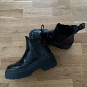 Svarta boots från Steve Madden med krokodilpräglat mönster - Säljer ett par svarta boots från Steve Madden med chunky platt sula och krokodilpräglat mönster. De är använda men väl omhändertagen också! 
