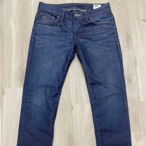 Mörkblå jeansbyxor från G-Star RAW - Snygga mörkblå jeans från G-Star RAW med klassisk femficksdesign och raka ben. Jeansen har dragkedjegylf och subtila sömdetaljer på bakfickorna. Perfekta för dig som gillar en stilren och tidlös look.