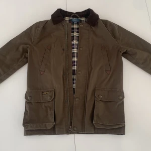Brun jacka från Polo Ralph Lauren - Snygg brun parkajacka från Polo Ralph Lauren med klassisk krage i manchester och rutigt foder. Jackan har stora fickor med knappar och dragkedja framtill. Perfekt för höst och vinter, med en tidlös look och sköna material. Nypris runt 6000
