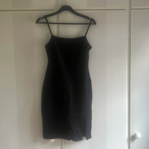 Svart tight klänning med smala axelband - Säljer en svart tight klänning med smala axelband och rak halsringning. Klänningen är kort och har en enkel, stilren design som passar perfekt till sommarens alla tillfällen.