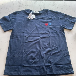 Mörkblå t-shirt från Comme des Garçons Play - Säljer en mörkblå t-shirt från Comme des Garçons Play med två broderade hjärtan på bröstet, ett rött och ett blått. Klassisk passform och rund halsringning. Perfekt för dig som gillar stilrena plagg med en twist. Pris kan diskuteras vid smidig affär
