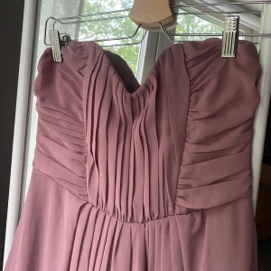 Axenbandslös balklänning  - Färgen syns bäst på första bilden. Den är typ syrenlila skulle jag säga. Säljer för att den tyvärr inte passar mig. Den har dragkedja där bak samt en ”klisterrem” där fram som gör att den inte riskerar att åka ner.  