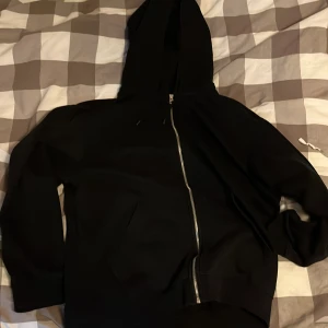 Svart hoodie med dragkedja från Weekday - Säljer en svart hoodie från Weekday i storlek M. Tröjan har dragkedja framtill, huva och två fickor. Sparsamt använd 