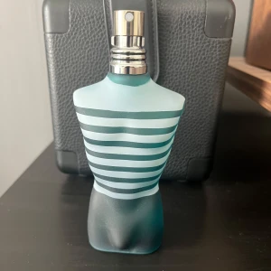  Jean Paul Gaultier - Le Male - Ikonisk parfymflaska formad som en manlig torso i frostat blått glas med vita och turkosa ränder. Metallisk spraytopp. Doften är känd för sin fräscha och sensuella karaktär. 75 ml använd ca 20 sprut.