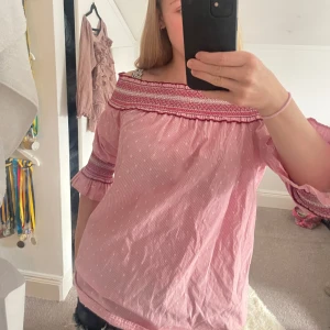 Rosa offshoulder blus från Primark - Säljer en söt rosa offshoulder blus från Primark med vita prickar och broderade detaljer i rött och vitt. Blusen har trekvartsärmar med volang och smock upptill och vid ärmslut. Perfekt för en chill och trendig look!💞💞💞💞 