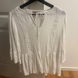 Vit boho-blus från KappAhl med knyt - Superfin vit blus från KappAhl i boho-stil med knytning vid halsen och dekorativa broderade detaljer framtill. Blusen har trekvartsärmar med volang och är tillverkad i ett lätt, luftigt bomullstyg. Perfekt för en chill och avslappnad look.