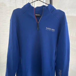 Blå Red Bull Racing tröja från Pepe Jeans - Snygg blå långärmad halvzip från Red Bull Racing x Pepe Jeans. Tröjan har sportig känsla och detaljer i rött och grått vid dragkedjan. Perfekt för dig som är Red bull racing intresserad. 