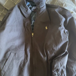 Mörkblå jacka från Polo Ralph Lauren - Säljer en klassisk mörkblå jacka från Polo Ralph Lauren med dragkedja och krage. Jackan har två snedställda fickor framtill. Perfekt för svalare dagar. Pris kan diskuteras