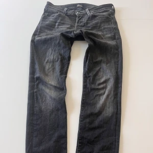 Svarta jeans - Säljer ett par svarta jeansbyxor med klassisk femficksdesign och diskreta slitningar framtill. Byxorna har raka ben och slim  passform, perfekta till vardags. Jättefint skick