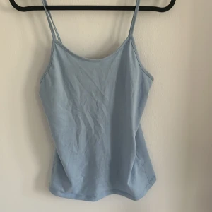 Ljusblå linnetopp från 157 - Säljer en ljusblå linnetopp från 157 med tunna axelband. Toppen är tillverkad i mjuk bomull med lite elastan för extra komfort. Perfekt för varma dagar eller som lager under andra plagg.