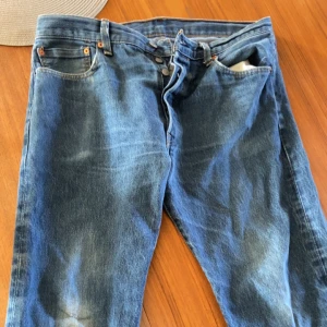 Levi's 501 jeans blå - Klassiska blå Levi's 501 jeans med raka ben och femficksdesign. Byxorna har knappgylf och tydlig Levi's-lapp bak i midjan. Lite sönder på märket där bak och småslitna byxor. Pris kan diskuteras