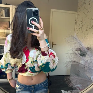 Blommig blus - Säljer en färgglad blommig croppad blus med ballongärmar. Blusen har v-ringning och resår vid ärmslut och midja. Perfekt till sommaren! Passar xs-m men det står M på toppen men passar mig som har xs💕