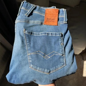 Replay Hyperflex jeans med slitningar - Snygga blå Replay Hyperflex jeans med slitna detaljer och lätt tvättad look. Klassisk femficksmodell med logotyp på bakfickan och läderpatch i midjan. Perfekta för en avslappnad stil.