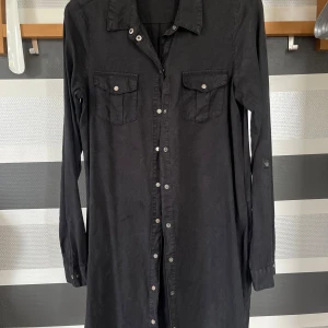 Svart skjortklänning från Vero Moda - Svart skjortklänning från Vero Moda med långa ärmar och knappar framtill. Använd ungefär 3 gånger. Nypris 549kr. Två bröstfickor med lock och knappdetaljer. Klassisk krage och rak passform, perfekt för en stilren look.