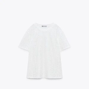 Vit t-shirt med broderade detaljer från Zara - Säljer en vit t-shirt från Zara med korta ärmar och broderade hål som ger en luftig känsla. Perfekt till sommaren och enkel att matcha med jeans eller kjol. Klassisk rund halsringning och normal passform.