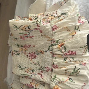 Blommig kortklänning med volang - Supersöt kortklänning i ljusbeige med blommigt mönster i rosa, grönt och gult