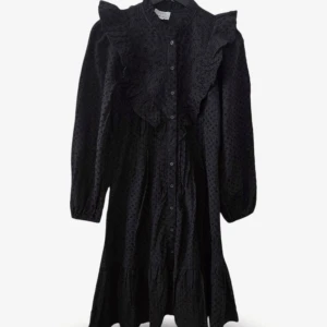 Svart volangklänning från & Other Stories - Elegant svart klänning från & Other Stories med diskret prickstruktur i tyget. Knäppning hela vägen framtill, volangdetaljer över axlar och byst samt en lätt A-linjeformad siluett. Vida ärmar med resår vid ärmslut och rynkad nederkant. Bekväm, luftig och enkel att styla – funkar både till vardag och fest.