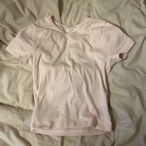 Ljusrosa basic mag tröja - Enkel och stilren ljusrosa t-shirt med korta ärmar och rund halsringning. T-shirten är i ett mjukt material och har en klassisk passform som funkar till det mesta. Perfekt för dig som gillar en clean och fräsch look.
