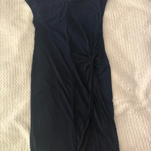 Mörkblå klänning från Vero Moda - Snygg mörkblå klänning från Vero Moda i figurnära modell. Klänningen har kort längd, draperad detalj i sidan och dragkedja bak. Perfekt för dig som gillar stilrena och enkla plagg med en twist. Materialet känns mjukt och följsamt.