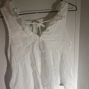 Vit volangblus med knyt i nacken - Supersöt vit blus i luftig bomull med volangdetaljer vid axlarna och v-ringning med knytband i nacken🤗Perfekt för varma dagar🥰