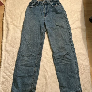 Blå high waist baggy jeans - Klassiska blå jeans med hög midja och baggy ben. Jeansen har fem fickor, dragkedja och knapp framtill. Tillverkade i denim med en avslappnad passform som ger en tidlös look.