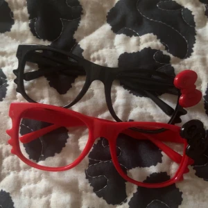 Hello Kitty glasögon i rött och svart - Två par Hello Kitty glasögon i plast, ett par röda och ett par svarta. Säljar båda för 30kr. Typ 12 cm 