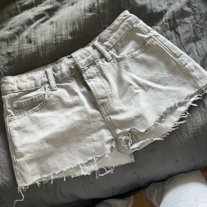 Grå jeansshorts med rå kant - Snygga grå jeansshorts med rå, fransig kant och klassisk femficksdesign. Shortsen har knappgylf och bälteshällor, perfekta för en avslappnad och trendig look. Passar dig som gillar en lite edgy stil och vill ha något som sticker ut i sommar.