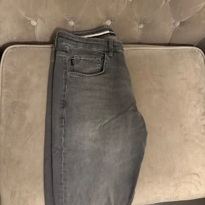 Grå jeans från BOSS - Snygga grå jeans från BOSS med klassisk femficksdesign och diskret logga på bakfickan. Jeansen har en lite baggy passform och är tillverkade i mjuk bomullsdenim med lite stretch för extra komfort. Perfekta för en clean och stilren look.