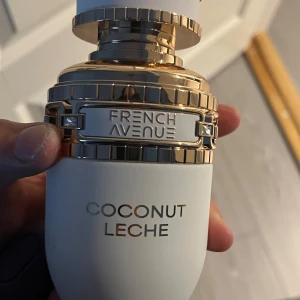 French Avenue Coconut Leche parfym - Lyxig parfymflaska i matt vit med detaljer i guld och silver. Doften heter Coconut Leche och flaskan har en modern, rundad form med exklusiv känsla. Perfekt för dig som gillar tropiska och krämiga doftnoter.
