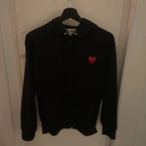 Svart hoodie från Comme des Garçons Play - Hej, jag säljer en svart hoodie från Comme des Garçons med det ikoniska röda hjärtat broderat på bröstet. Tröjan är väldigt bekväm och i toppskick då den inte har nå defekter eller fläckar. Pris kan diskuteras! 
