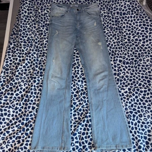 Ljusblå bootcut jeans från Pull&Bear - Säljer ett par ljusblå jeans från Pull&Bear med bootcut passform. Jeansen har slitna detaljer framtill, klassiska fickor bak med knapp och låg midja. De är använda få gånger