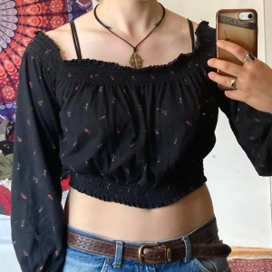 Svart blommig offshoulder blus från H&M, M - Supersöt svart offshoulder blus med små röda rosor på. Croppad modell med resår i midjan och vid halsringning. Långa ärmar med resår vid handlederna. Perfekt för sommaren! Superskönt material, bomull. Var min absoluta favoritröja ett tag, men använder tyvärr för sällan nu!