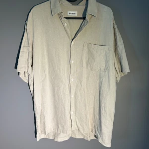 Beige kortärmad skjorta från Weekday - Säljer en stilren beige skjorta från Weekday med korta ärmar och klassisk krage. Skjortan har knäppning framtill och en bröstficka. Perfekt för en avslappnad look.