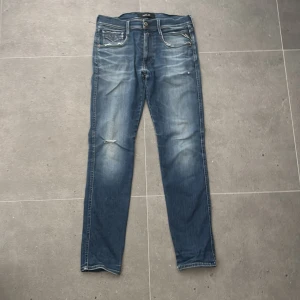 Blå Replay jeans slim fit - Säljer ett par blå jeans från Replay i klassisk slim fit. Jeansen har snygga slitningar och ljusare partier framtill, fem fickor och normal midja. Materialet är robust denim som ger en cool och avslappnad look. W31 L32. Modell: Anbass. Fickorna har viss töjning, och finns små hål på vissa ställen - priset är satt därefter 
