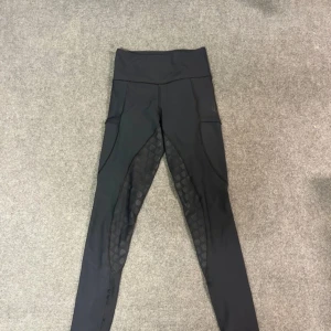 Svarta ridleggings med grepp - Snygga svarta ridleggings från Mountain Horse med hög midja och silikon-grepp på insidan av benen. Stretchigt material som sitter tight och har praktiska fickor på sidorna. Perfekta för ridning och träning.