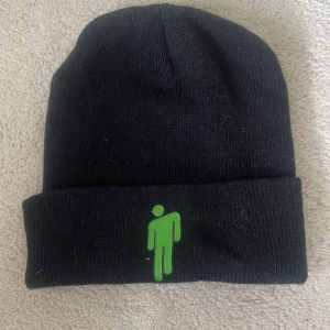 Svart Billie Eilish mössa - Svart ribbstickad mössa med uppvikt kant och en grön logga framtill. Pris kan sänksas.