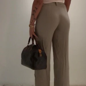 Olivgrön/begie raka kostymbyxor i linne - Snygga beiga kostymbyxor i linne med rak passform och midwaist. Byxorna har klassisk look med bälteshällor och stängs med dragkedja och knapp. Perfekta för en clean och stilren outfit.