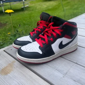 Nike Air Jordan 1 Mid svart/vit/röd - Säljer ett par Nike Air Jordan 1 Mid med klassisk svart, vit och röd färgkombination. Använder ej längre