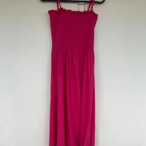 Rosa långklänning från H&M XS - Superfin långklänning i stark rosa från H&M. Klänningen har smock upptill, tunna axelband och volangkant vid bysten. Lätt och luftig modell som passar perfekt till varma dagar. Materialet är mjukt och känns bekvämt mot huden. De går även perfekt att vicka ner som en kjol!
