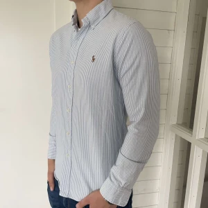Ralph lauren skjorta - En riktigt snygg randig ralph lauren skjorta perfekt till sommaren. Skjortan är i storlek M  slim fit och den är 74 cm lång och 49 cm bred. Den är i mycket bra skick, hör av er vid frågor.