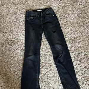 Svarta bootcut jeans från Gina Tricot - Snygga svarta bootcut jeans från Gina Tricot med slitna detaljer på låren. Jeansen har klassisk femficksdesign, silverfärgade knappar och dragkedja. Materialet är jeans med en mörk tvätt och coola slitningar för en trendig look.