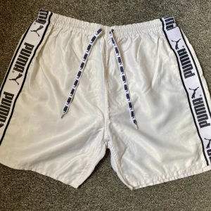 Retro vita shorts från Puma med logga - Klassiska Puma shorts i glansigt material, använda men i bra skick för åldern. Se bilder för egen bedömning. Storlek XL.
